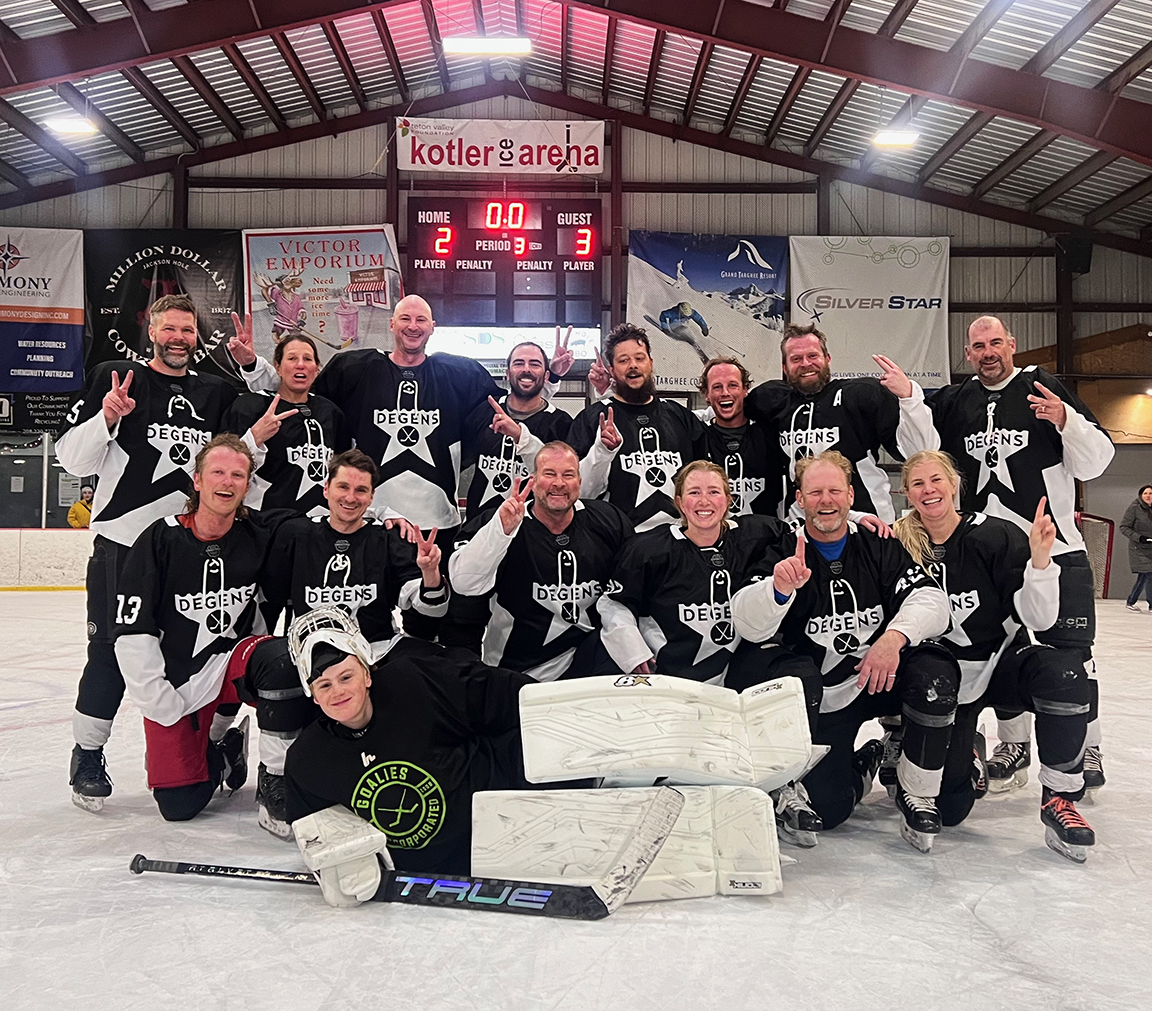 Group of hockey players in black-and-white jerseys posing on the rink after a game, making victory signs together.